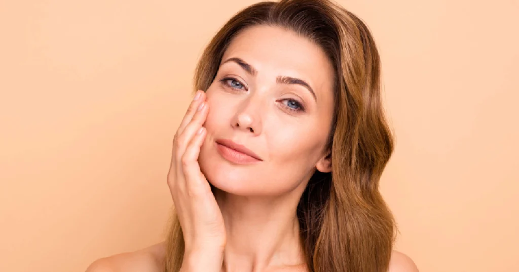 Woman with clear, glowing skin gently touching her face, representing the results of a HydraFacial in Frederick, MD
